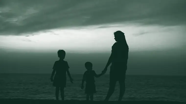 Una madre y sus dos hijos de la mano frente al mar, a contraluz